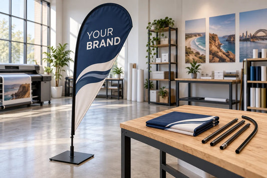 Navy teardrop banner on a square base beside folded printed fabric and separate pole sections in a studio.
